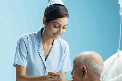 A nurse helping an older patient eat at his hospital bed