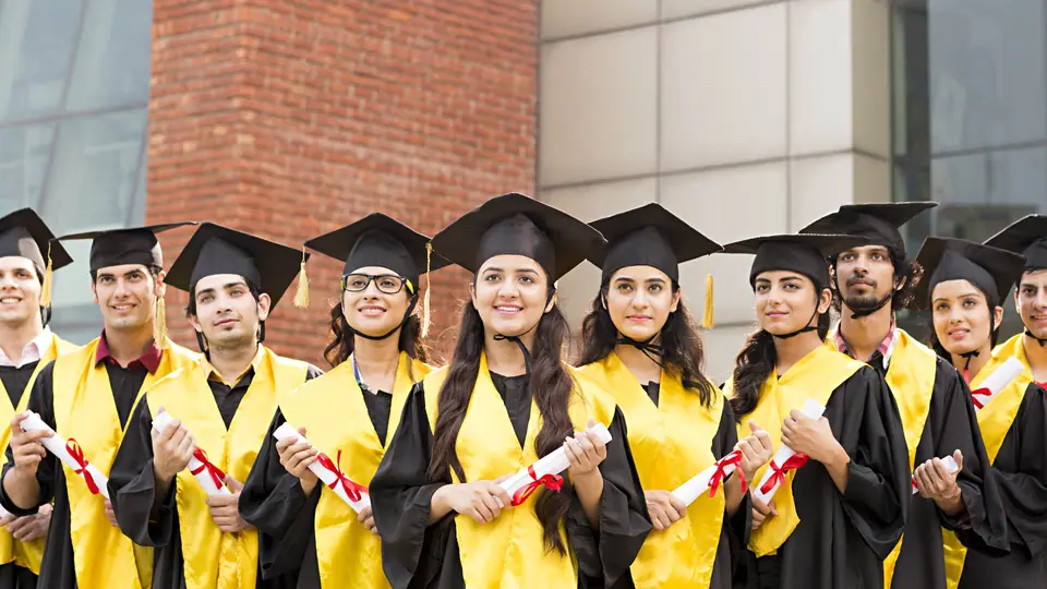 Graduates in caps and gowns holding certificates outside a college building