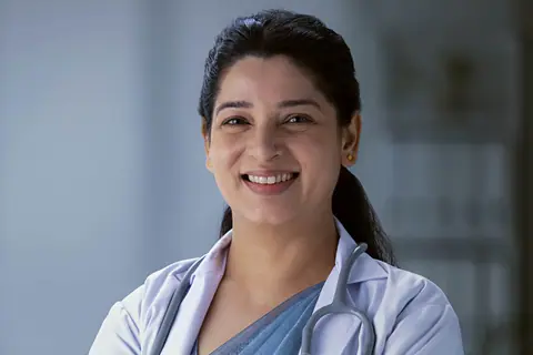 A smiling nurse in a white coat, stethoscope round her neck, arms folded
