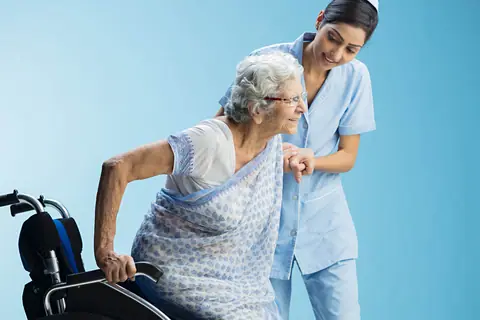 A nurse helping an older woman stand up from a wheelchair