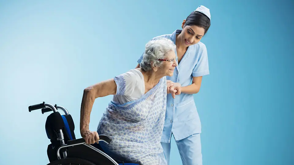 A nurse helping an older woman stand up from a wheelchair