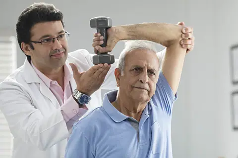 A physiotherapist helping an older man raise a small dumbbell above his head