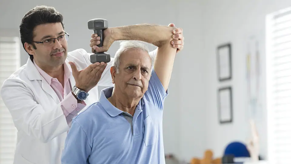 A physiotherapist helping an older man raise a small dumbbell above his head