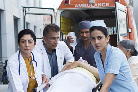 Doctors, a paramedic and a nurse wheeling a patient on a trolley away from an ambulance