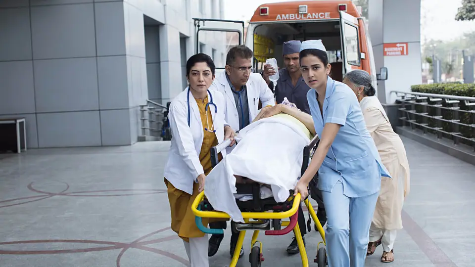 Doctors, a paramedic and a nurse wheeling a patient on a trolley away from an ambulance