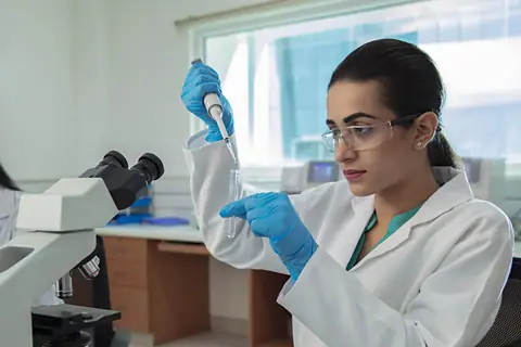 A student pipetting a sample into a test tube in a laboratory, another at a microscope