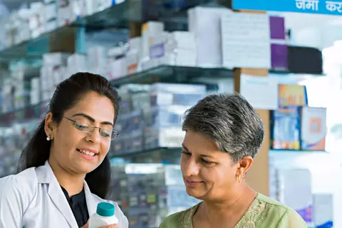 A pharmacist explaining a medicine bottle to a customer at the counter