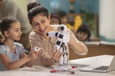 A teacher showing a small robot to a girl at a classroom table