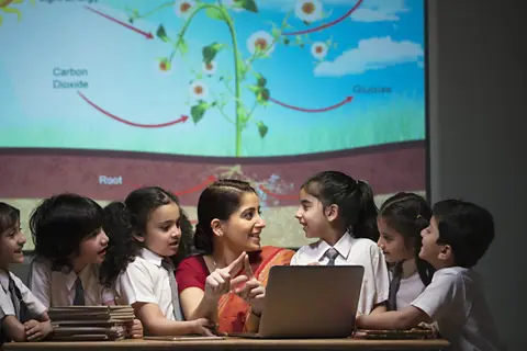 A teacher talking with a group of primary school children around a laptop