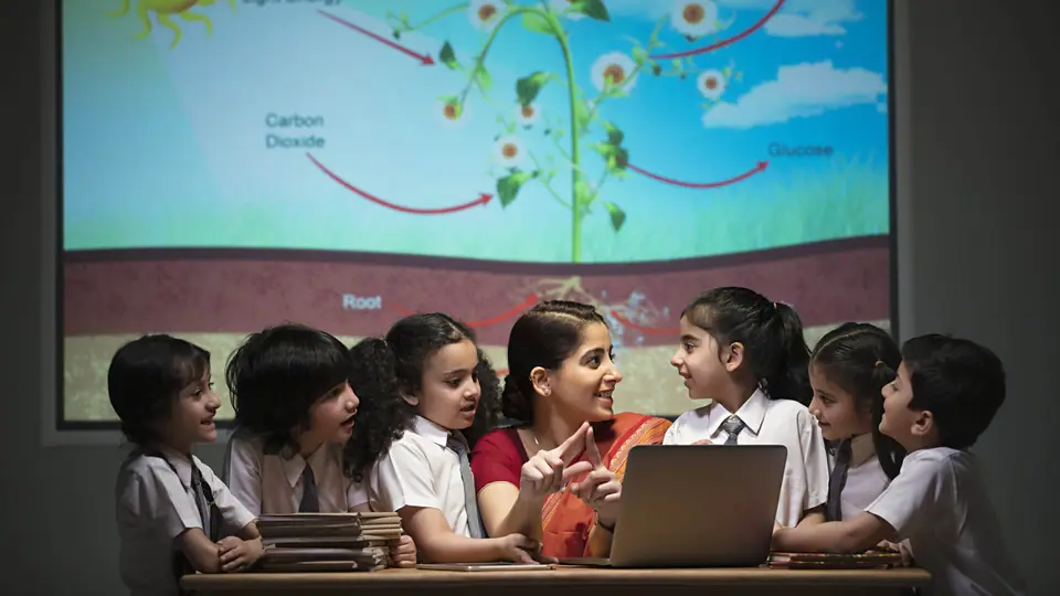A teacher talking with a group of primary school children around a laptop