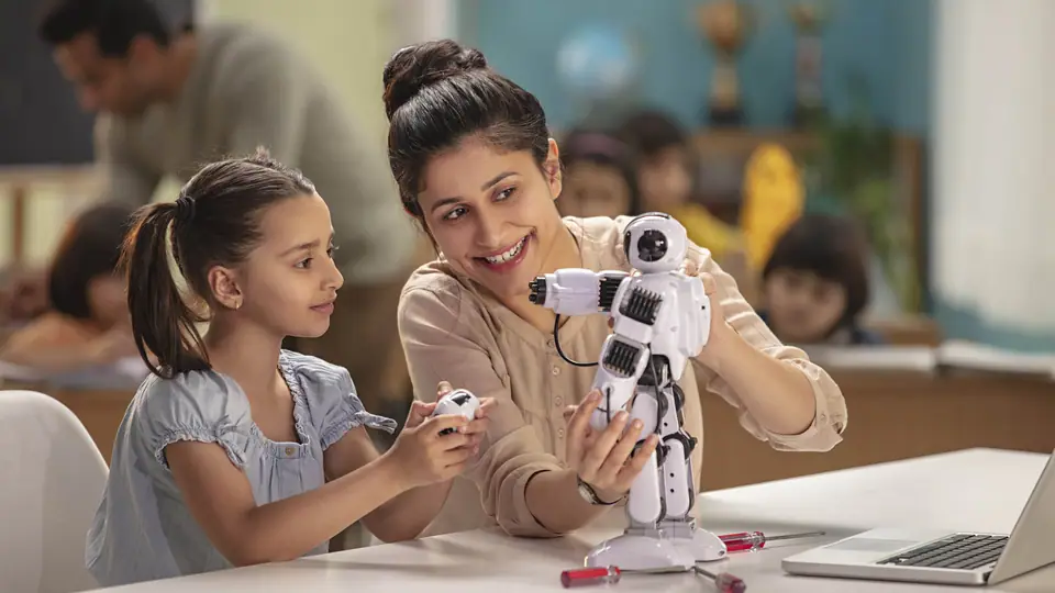 A teacher showing a small robot to a girl at a classroom table